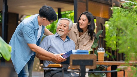 asian couple surprised elderly father with birthday gift at outdoor cafe restaurant on summer holiday vacation. family relationship, celebrating father's day and older people health care concept.