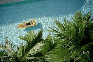 enjoying suntan. tropical vacation concept. top view of young woman on the yellow air mattress in the swimming pool with palm trees.