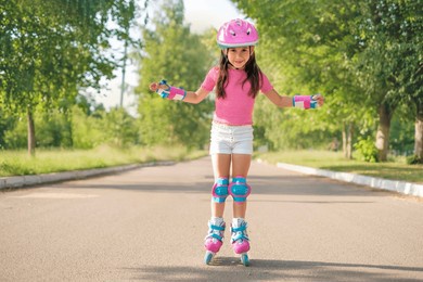 a beautiful preschool girl in a protective sports helmet and roller skates rides on an asphalt path on a hot summer morning.  the child learns new skills and learns sports