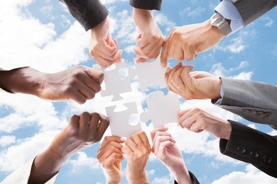 directly below shot of multiethnic business people assembling jigsaw puzzle against sky