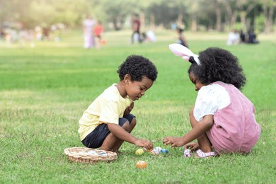 little african boy and girl wearing bunny ears pick up easter egg in garden, easter eggs hunting outdoors