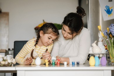 cute little girl with her mother preparing for painting easter eggs. mom and daughter in apron
