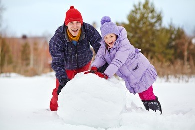 funny dad and daughter with a snowman. family walking outdoors in winter