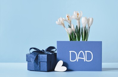 small luxury gift box with blue bow and white heart. dad text on gift card and white crocus flowers. fathers day or birthday gift for him. festive sale