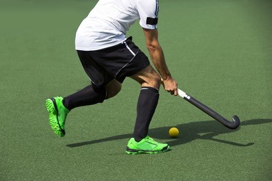 field hockey player, in possesion of the ball, running over an astroturf pitch, looking for a team mate to pass to