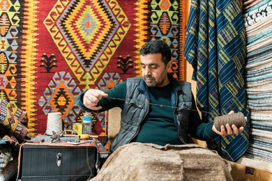 ethnic middle aged man sitting in store sewing and fixing carpet