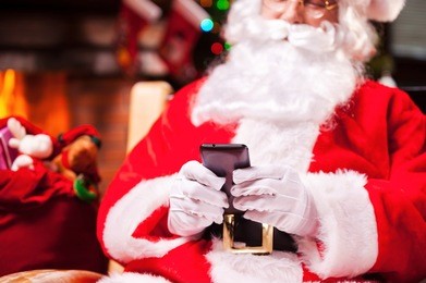 santa claus texting. close-up of happy santa claus typing message on the mobile phone and smiling while sitting at his chair 