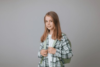 cheerful teenage girl 11,12,13 years old in a school uniform wears a backpack on a gray background. school fashion