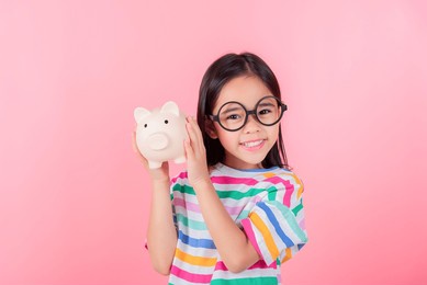 little asian girl saving money in a piggy bank, learning about saving, kid save money for future education. money, finances, insurance, and people concept