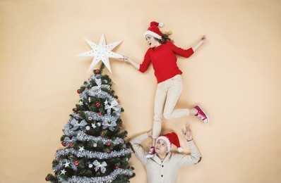 happy young couple decorating christmas tree against the beige background
