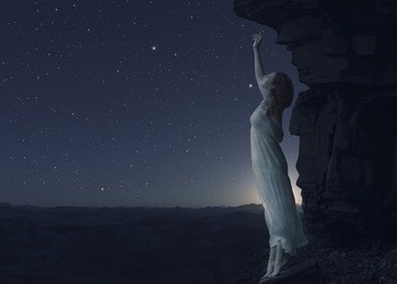 young woman standing on cliff's edge of another planet and looks into the distance.