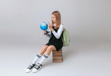 schoolgirl isolated on yellow background with globe. little girl in school uniform sitting on a yellow background, reading a book. blonde girl in school uniform on a yellow background