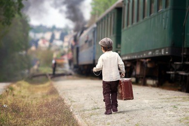 boy, dressed in vintage shirt and hat, with suitcase, on a railway station, steam train