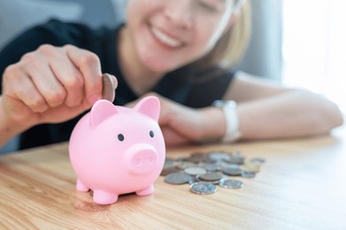 happiness woman while putting a coin into piggy bank for saving money. a piggy bank is a small container used to save coins, often but not always shaped like a pig.