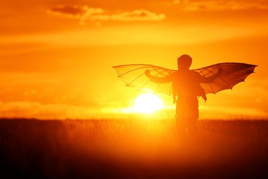 child silhouette with wings at sunset. funny kid run in the meadow on a summer evening. boy dream of flying and imagine themselves as pilots.
