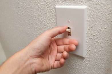 hand turning wall light switch off