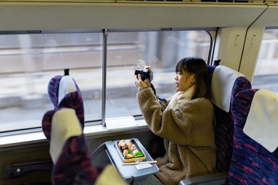 young asian woman using digital camera taking picture of beautiful view out of the window during travel on train at sunset. attractive girl travel japan on railroad transportation on winter vacation.