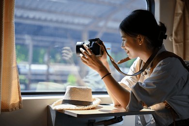 a happy and beautiful young asian female traveler sits at her seat and takes a picture from the train with her camera. summer vacation, journey, solo traveler