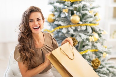 happy young woman opening shopping bag near christmas tree