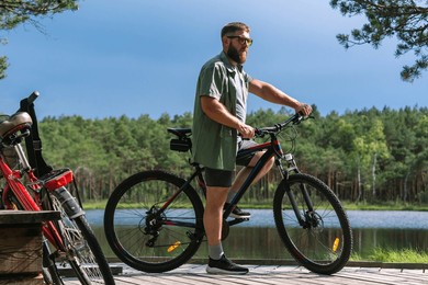 satisfied smiling happy bearded man in casual green jacket jeans riding bicycle bike on sidewalk in park outdoors, look camera. people active urban healthy lifestyle cycling concept.