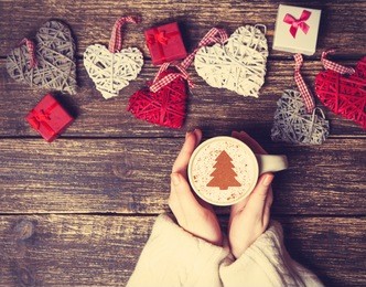 female holding cup of coffee with cream christmas tree on a table.