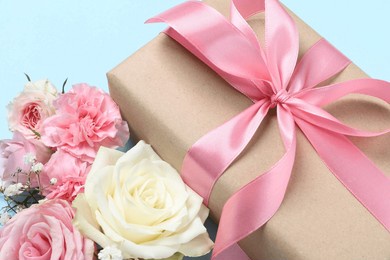 gift box and beautiful flowers on light blue background, closeup