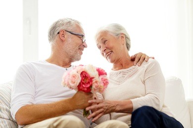 family, holidays, age and people concept - happy senior couple with bunch of flowers at home
