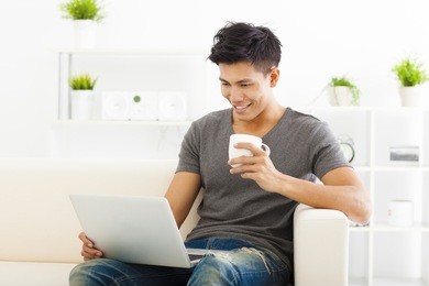 happy young man sitting in sofa and using  laptop