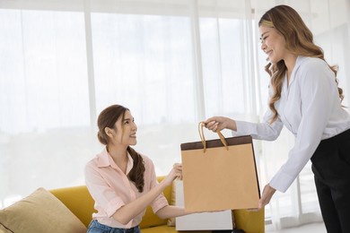 happy asian salesperson giving shopping bag to satisfied woman customer at trendy retail store - consumerism and shopping concept