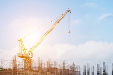 building site with high-rise block under construction in an urban environment dominated by a large industrial crane silhouetted against a cloudy blue sky