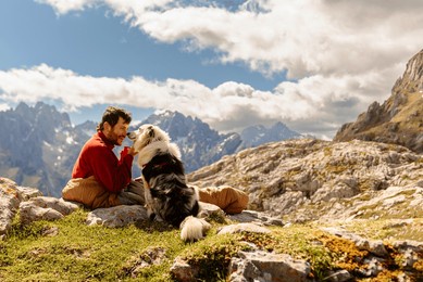 bearded white man, mountaineer, having coffee for breakfast inside a sleeping bag after bivouacing in the mountains with his border collie dog. traveling with a pet. sport and adventure.