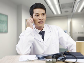 young asian doctor taking a phone call  looking shocked.