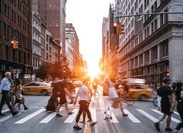people, cars, taxis and bikes in the busy intersection of 5th avenue and 23rd street in new york city with summer sunset shining between the background buildings