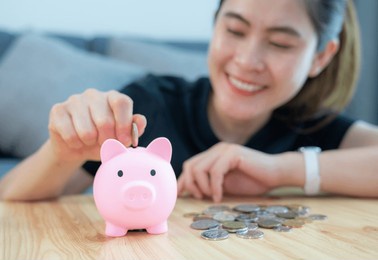 happiness woman while putting a coin into piggy bank for saving money. a piggy bank is a small container used to save coins, often but not always shaped like a pig.