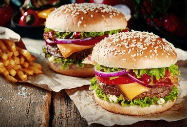 two cheeseburgers on sesame buns with succulent beef patties and fresh salad ingredients served with french fries on crumpled brown paper on a rustic wood table