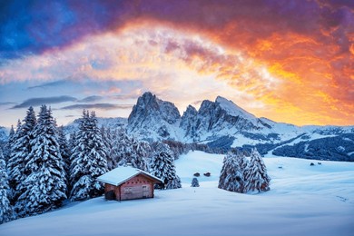 picturesque landscape with small wooden log cabin on meadow alpe di siusi on sunset time. seiser alm, dolomites, italy. snowy hills with orange larch and sassolungo and langkofel mountains group