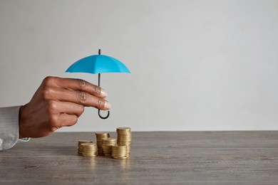 close up of african american woman hand holding blue umbrella over stack of coins on table. hands of financial advisor saving money. businesswoman protect saving and money with copy space.