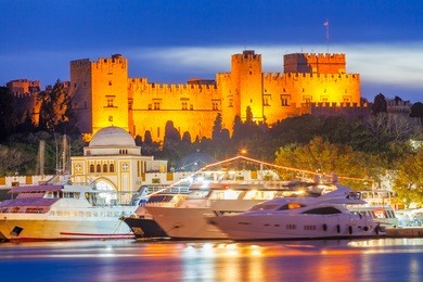 mandraki harbour rhodes greece and the palace of the grand master of the knights of rhodes at night.