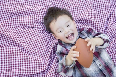 cute young mixed race boy playing with football outside on picnic blanket.