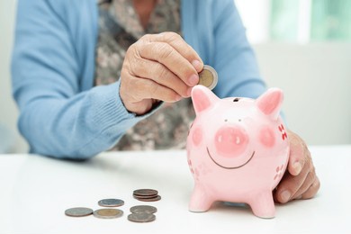 asian elderly woman putting coin into pink piggy bank for saving money and insurance, poverty, financial problem in retirement.