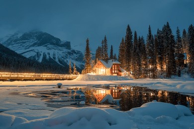 beautiful view of emerald lake with snow covered and wooden lodge glowing in rocky mountains and pine forest on winter at yoho national park, british columbia, canada