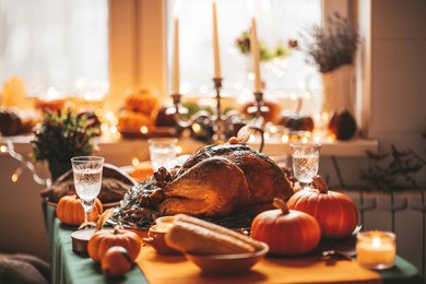 thanksgiving day dinner with holiday autumn decor and candles. family dining room table set with delicious golden roasted turkey on platter garnished rosemary fresh small pumpkins