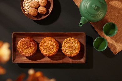 top view of tea table party with mooncakes and nuts on wooden tray and set of tea on black background. mid-autumn festival is an important and colorful traditional festival