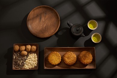 top view of wooden trays containing mooncakes and different seeds decorated on black background. chinese mid-autumn festival concept. advertising photo
