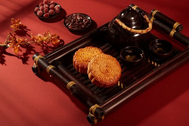 a tray featured two mooncakes and tea set arranged on red background with dishes of jam candies and melon seeds. mooncake for mid-autumn festival holiday