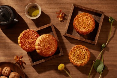baked mooncakes placed inside few wooden tray square-shaped. a dish of walnuts arranged. beautiful various mooncakes prepared for mid autumn festival