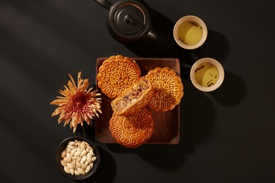 mooncake cut in half with green rice and coconut filling. a small dish pumpkin seeds displayed with black tea set. black background for traditional food promotion