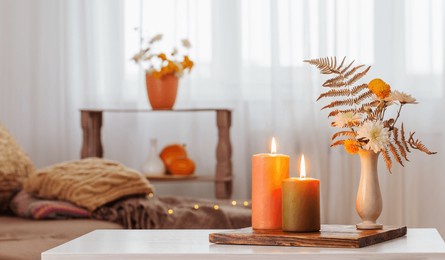 burning candles with autumn decor on white table at home