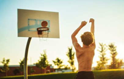 a kid boy playing basketball view from back on sunset