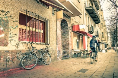 vintage retro travel postcard of a narrow street in the former east side of berlin - mix of past and present in the multicultural capital of germany - everyday life with people and bike on the road